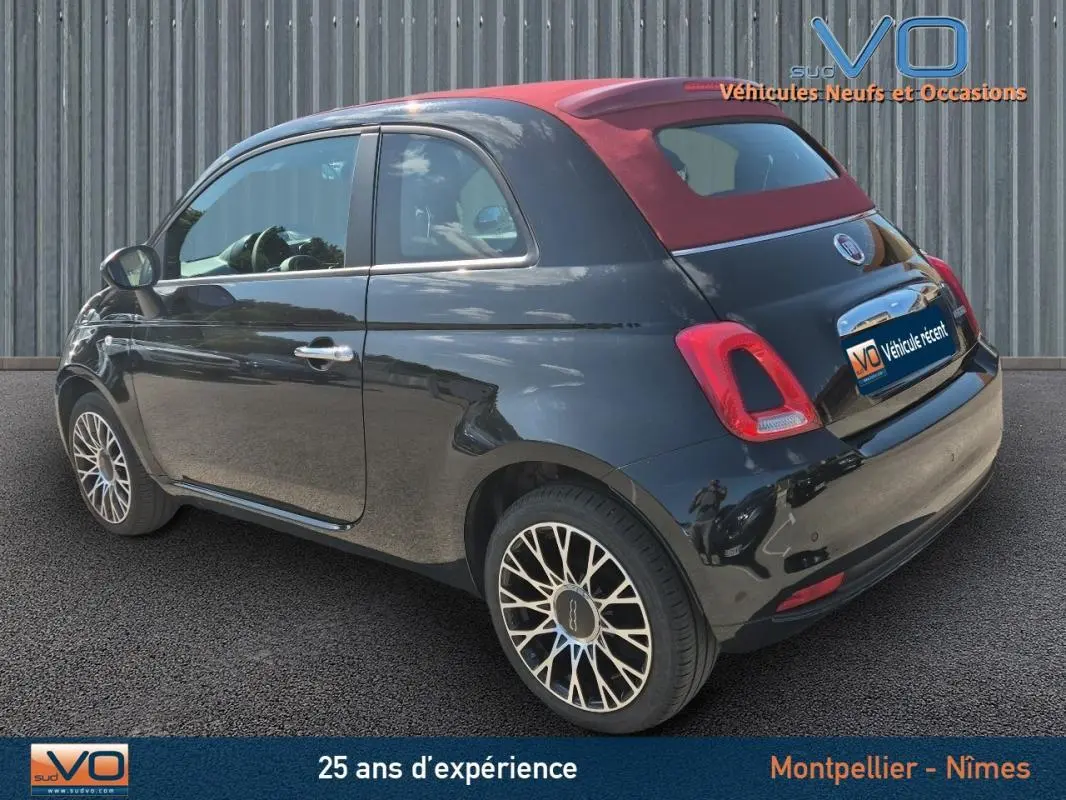 Vue 3/4 arrière droite d'une FIAT 500C noire avec toit rouge, roue de secours visible, modèle 2024 hybride essence.