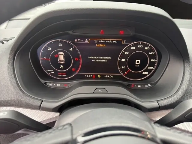Vue rapprochée du tableau de bord numérique de l'Audi Q2 30 TDI 116 Design, affichant la vitesse à 0 km/h et les alertes audio.