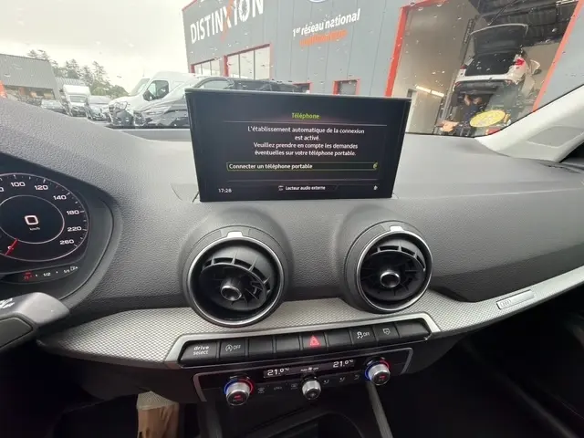 Vue intérieure du tableau de bord de l'Audi Q2 blanc 30 TDI 116 Design de 2021, avec écran tactile central et aérateurs ronds.