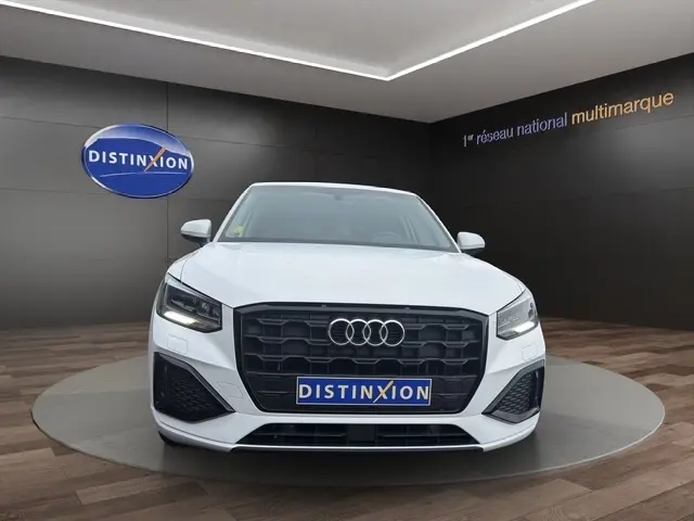 Audi Q2 blanc en 3/4 avant droit, avec calandre noire et jantes alliage, dans un showroom intérieur.