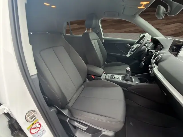 Vue intérieure côté conducteur de l'Audi Q2 blanc 30 TDI 116 Design, sièges tissu gris et tableau de bord moderne.