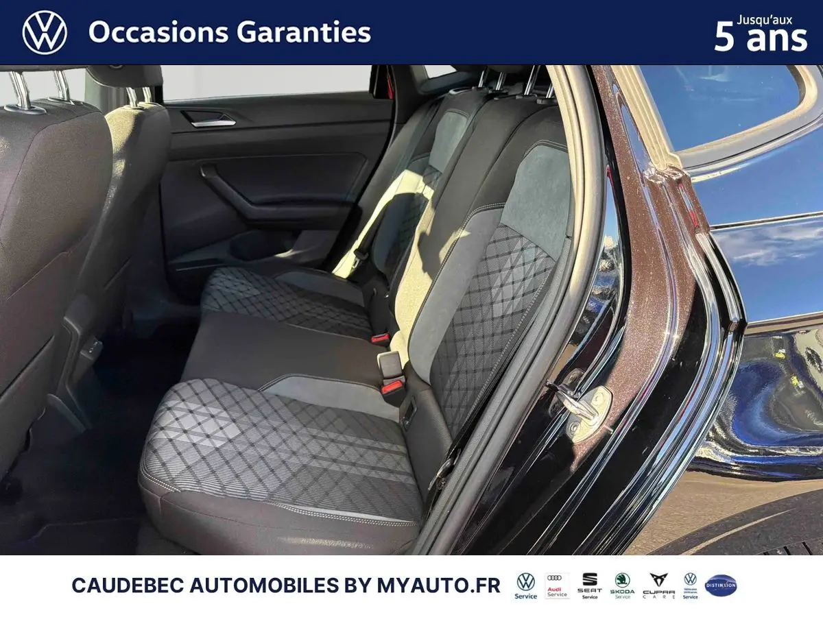 Vue côté droit sur l'intérieur arrière de la Volkswagen Polo noir intense nacré, montrant la banquette avec sellerie bicolore et motifs géométriques.