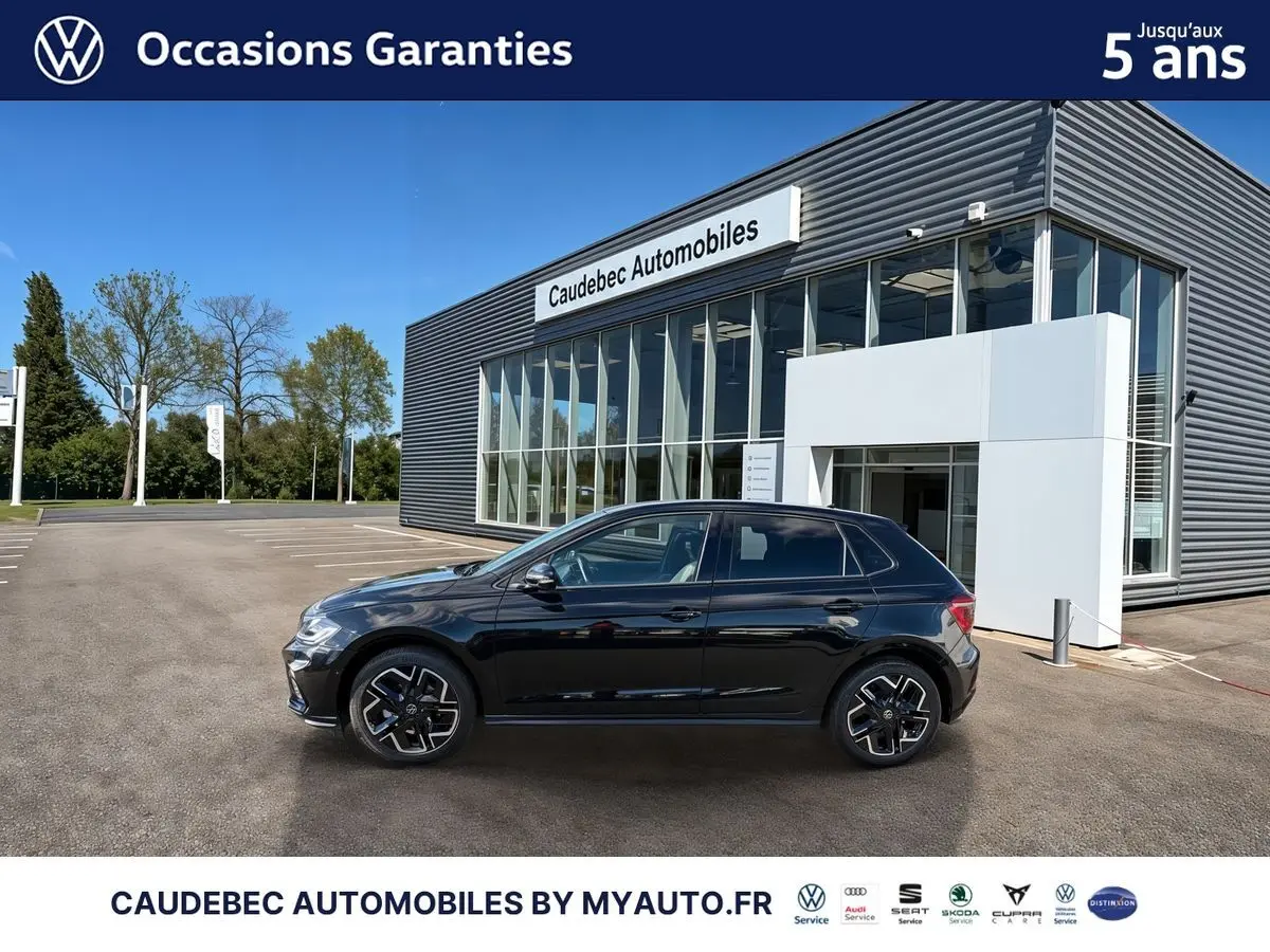 Vue latérale droite d'une Volkswagen Polo noire intense nacrée stationnée devant un bâtiment moderne en verre.