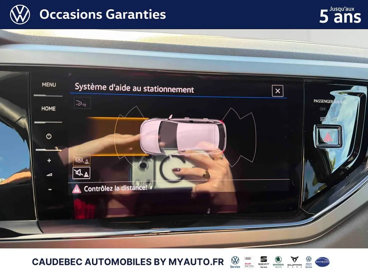 Écran tactile intérieur affichant le système d'aide au stationnement d'une Volkswagen Polo noire, vue de face.