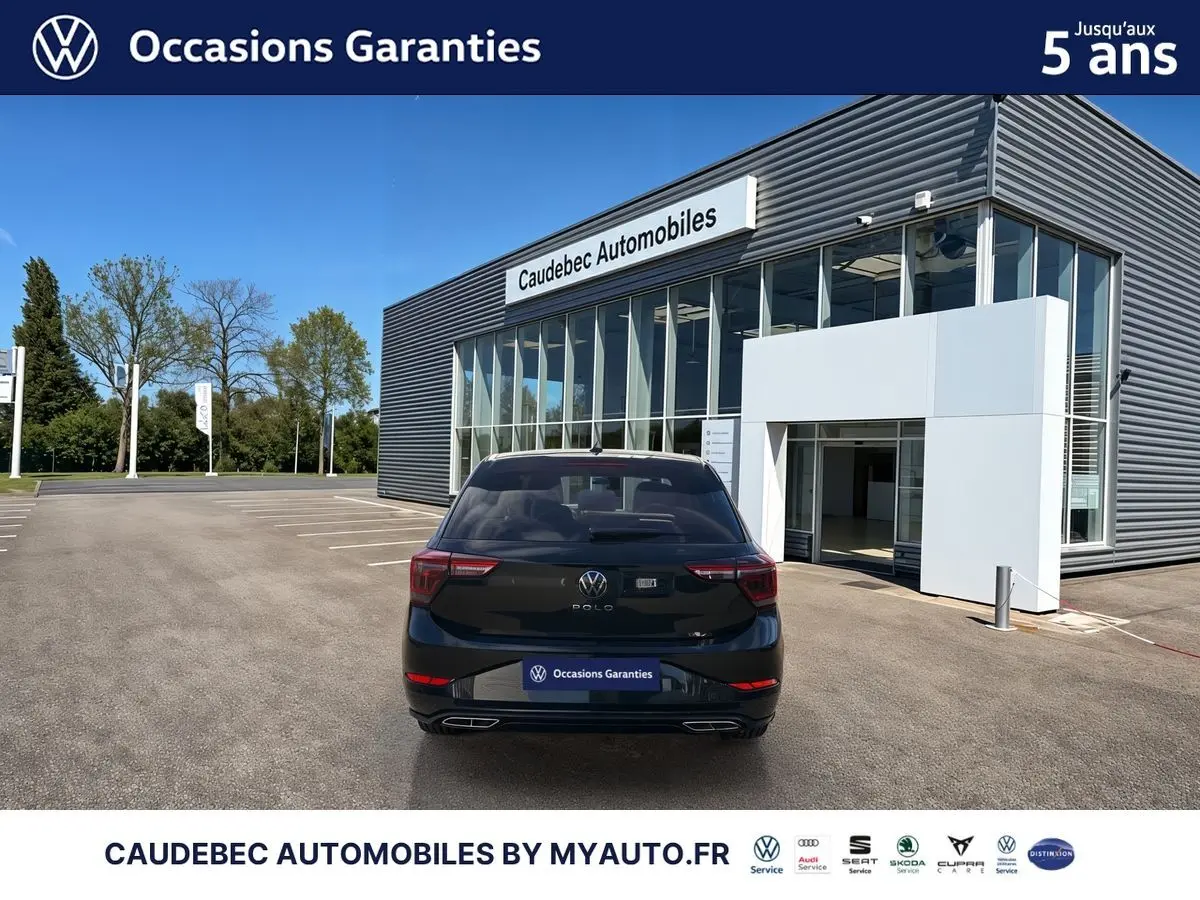 Vue arrière d'une Volkswagen Polo noire intense nacrée stationnée devant un bâtiment moderne de concession.