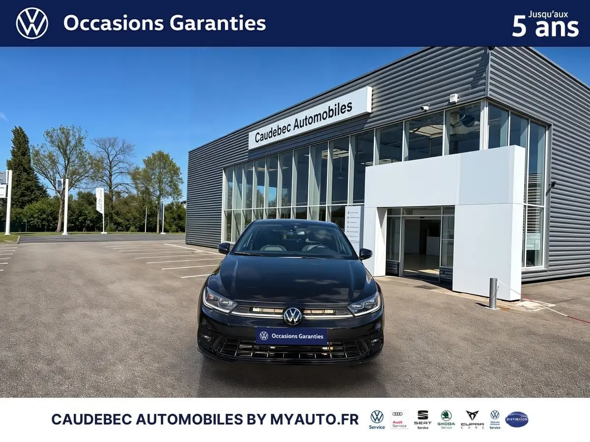 Vue frontale d'une Volkswagen Polo noire intense nacrée garée devant un bâtiment moderne de concession automobile.