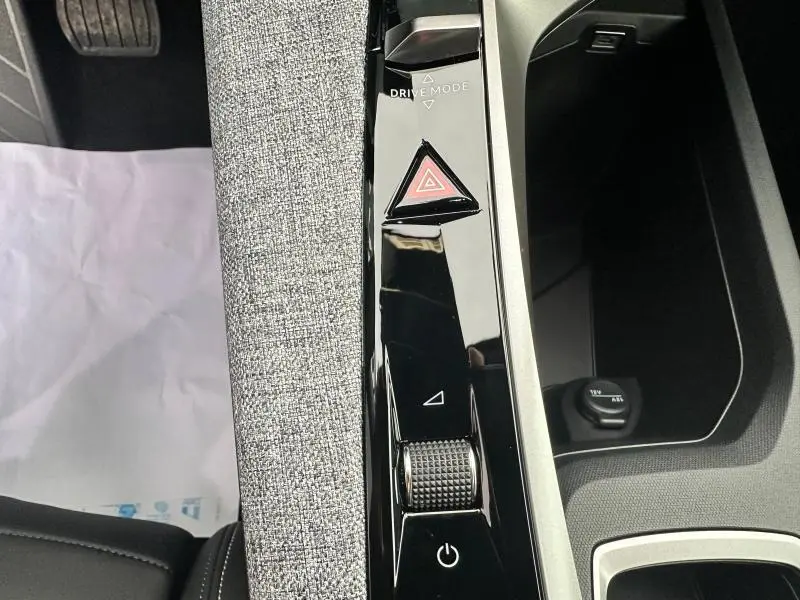 Vue rapprochée de la console centrale noire brillante avec bouton triangle rouge d'alerte et tissu gris dans un Peugeot 3008 2025.