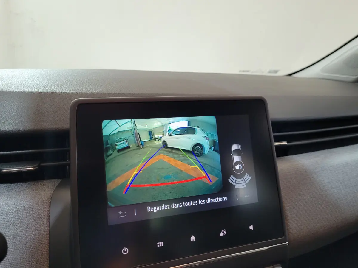 Écran tactile central montrant la caméra de recul d'une Renault Clio gris foncé avec lignes de guidage colorées.