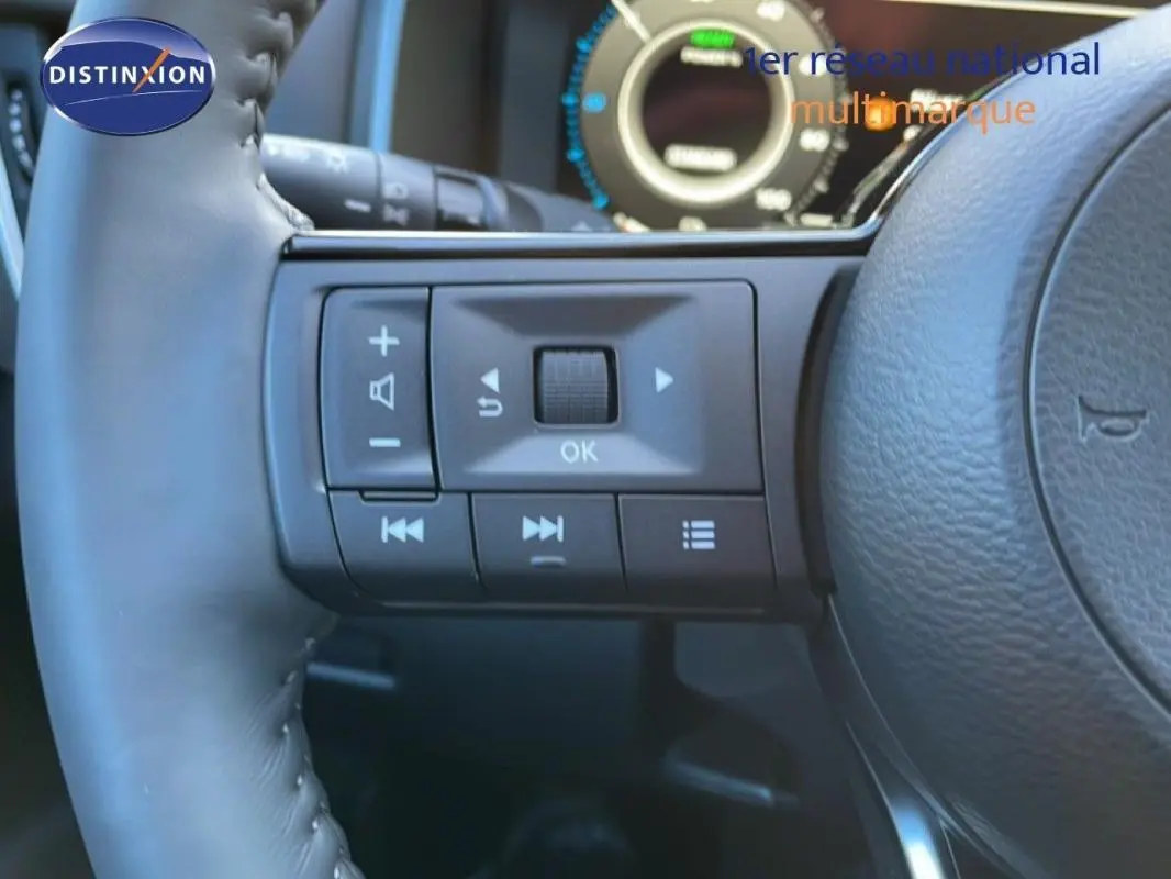 Gros plan sur les commandes gauche du volant cuir du Nissan Qashqai gris 2025 avec cockpit numérique en arrière-plan.