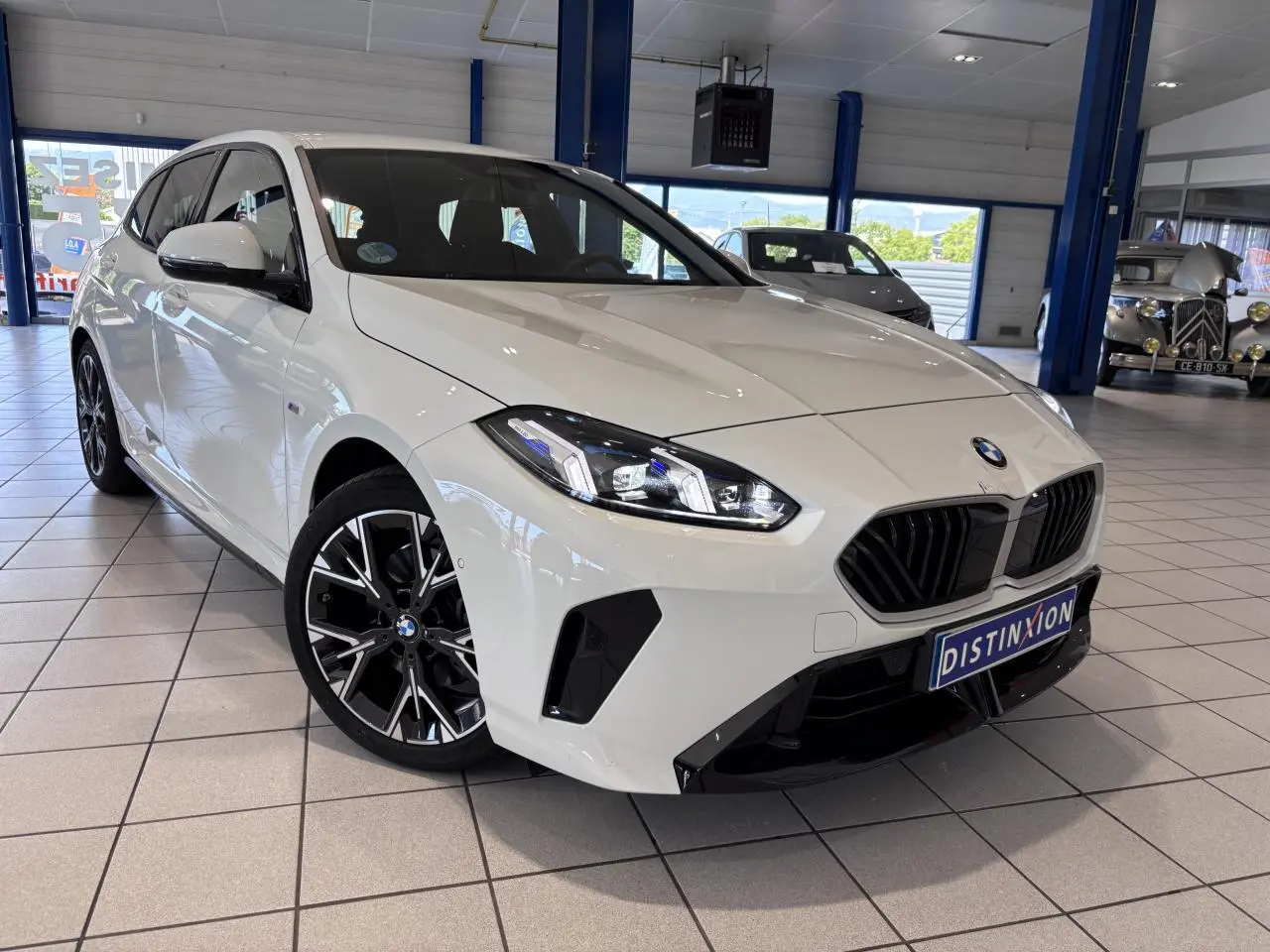 BMW Série 1 120d M Sport blanche vue en 3/4 avant droit, avec jantes noires et calandre noire distinctive.