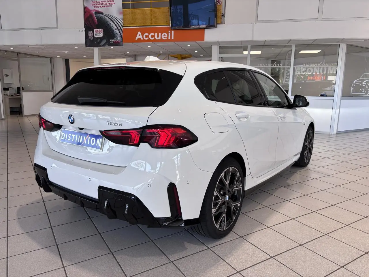 BMW Série 1 120d M Sport blanc vue 3/4 arrière droit en showroom, avec jantes noires et détails noirs contrastants.