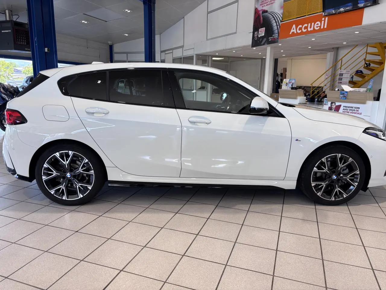 BMW Série 1 120d M Sport blanc vue de profil côté gauche en intérieur, avec jantes alliage noires et détails M Sport.