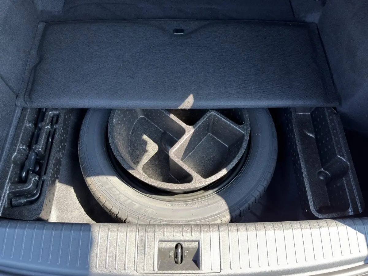 Vue du coffre ouvert d'une Renault Rafale noir, montrant la roue de secours et les compartiments de rangement sous la tablette.