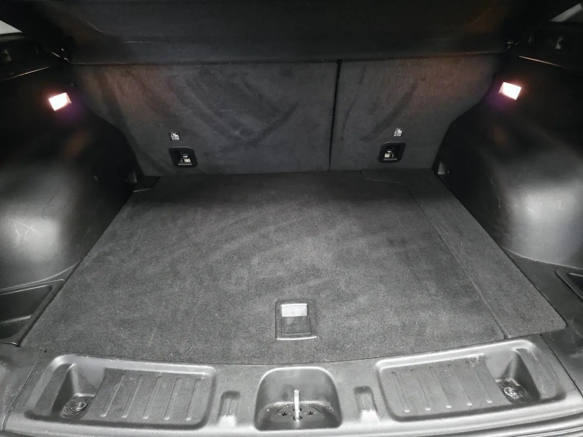 Coffre spacieux et noir du Jeep Compass 2024 hybride rechargeable, éclairé par deux lampes intérieures.