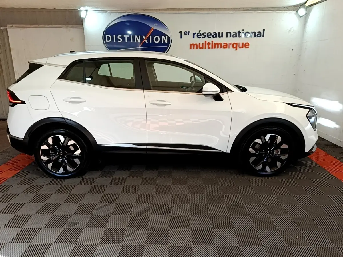Vue de profil côté gauche d’un KIA SPORTAGE blanc 2022 hybride rechargeable avec jantes noires et rails de toit noirs.