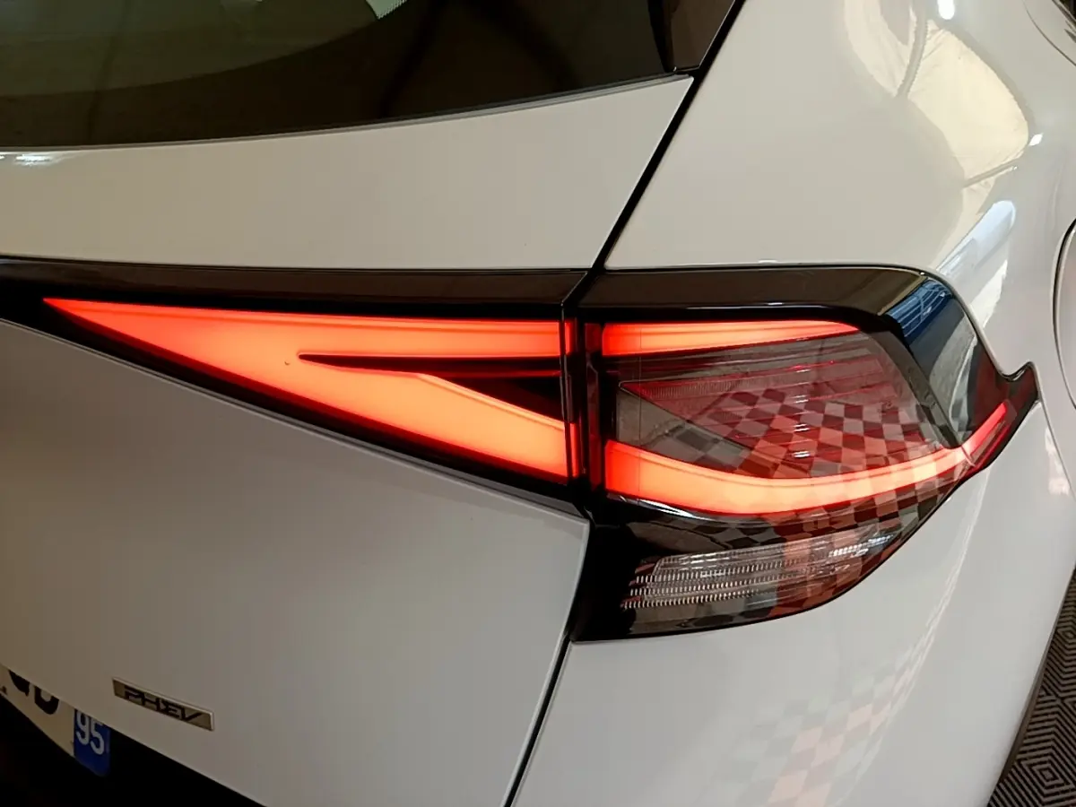 Gros plan sur le feu arrière droit allumé d’un KIA SPORTAGE blanc hybride rechargeable, détail du design lumineux moderne.