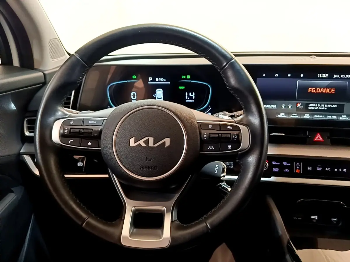 Vue intérieure centrée sur le volant cuir KIA et le tableau de bord numérique avec écran tactile du Kia Sportage blanc 2022.