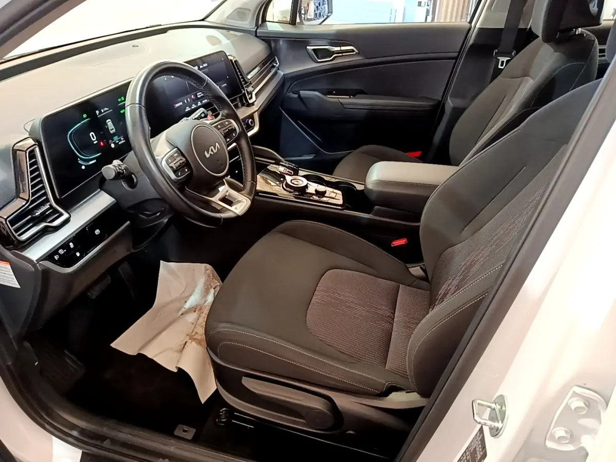 Intérieur côté conducteur du Kia Sportage blanc 2022, avec tableau de bord digital et sièges noirs en tissu.