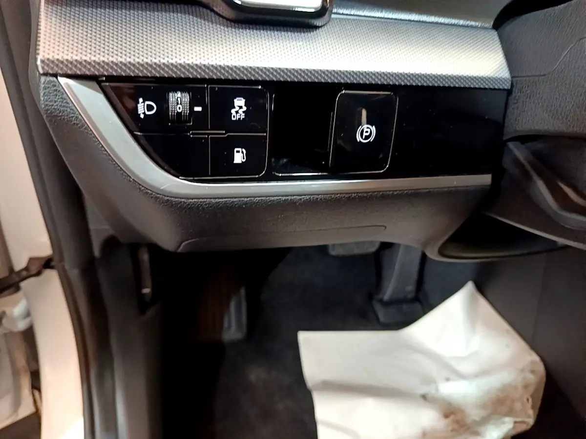 Détail intérieur côté conducteur du Kia Sportage blanc 2022 montrant les commandes d’éclairage et frein à main électrique.