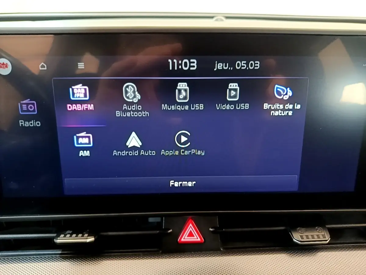 Écran tactile central du tableau de bord du Kia Sportage blanc, affichant les options multimédias et connectivité.