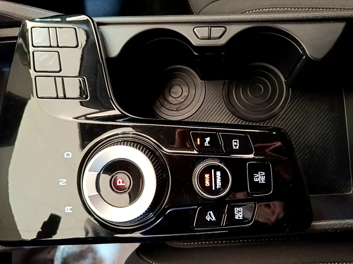 Gros plan sur la console centrale noire du Kia Sportage hybride rechargeable, avec sélecteur rotatif de boîte auto et boutons de contrôle.