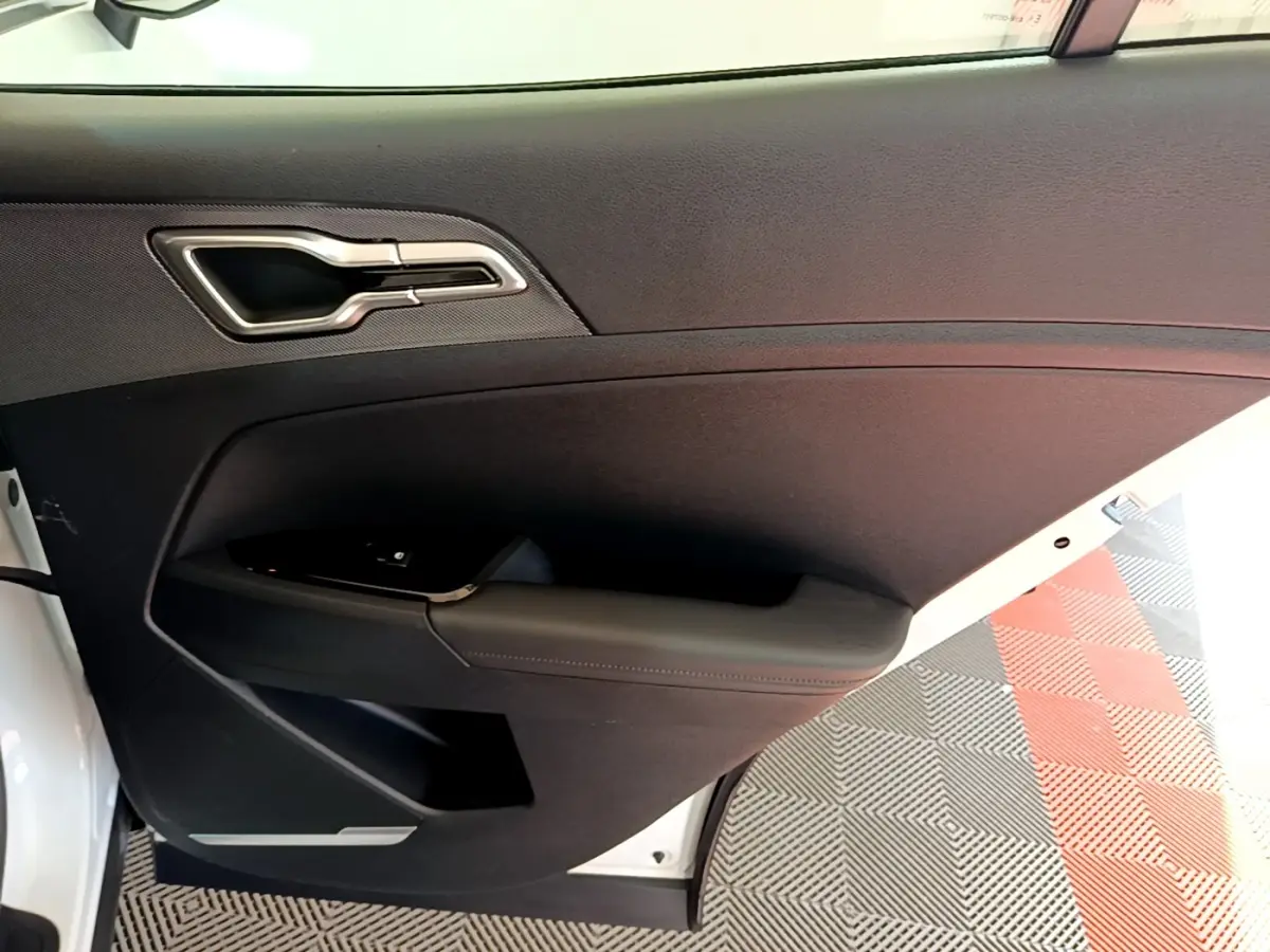 Vue intérieure côté gauche de la porte avant d’un KIA SPORTAGE blanc avec poignée argentée et accoudoir noir.