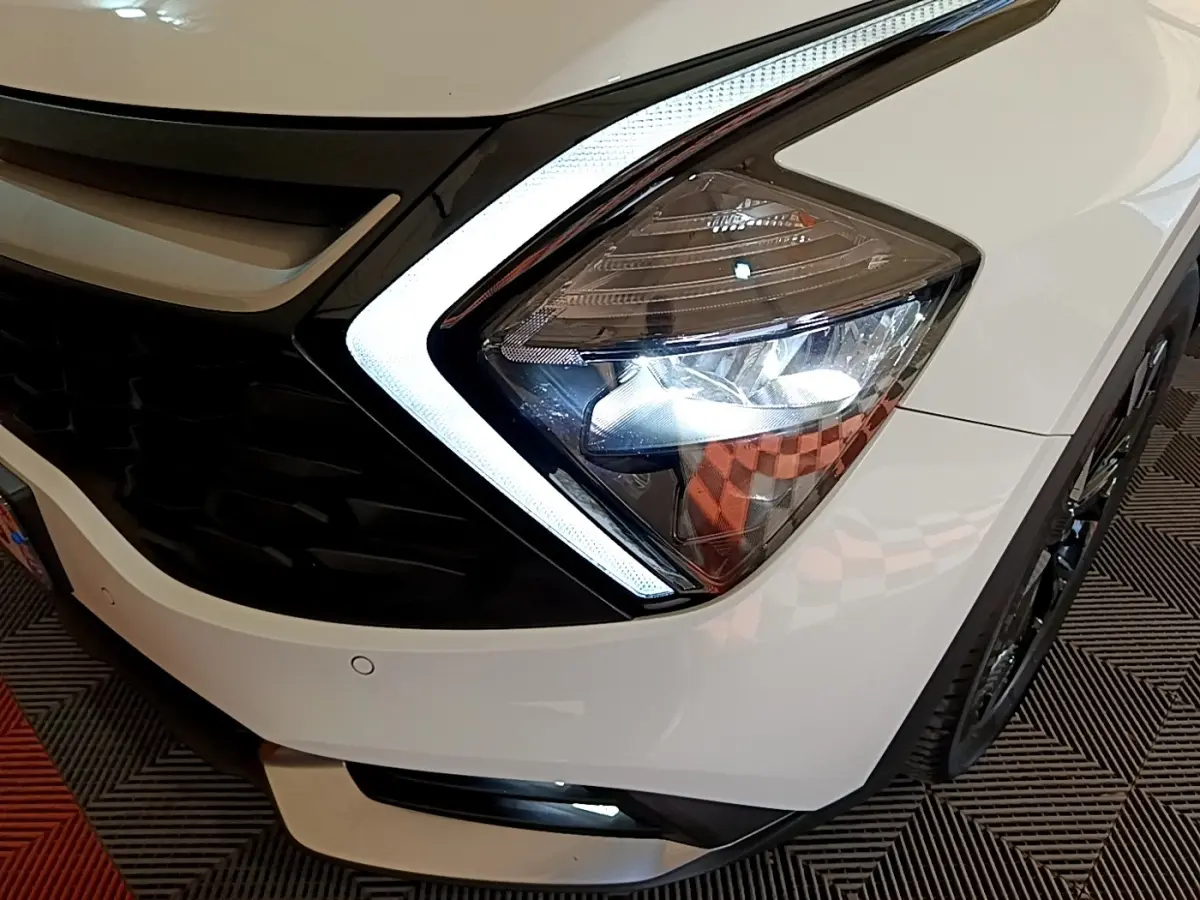 Gros plan sur le phare avant droit blanc du KIA SPORTAGE 2022 avec éclairage LED et calandre noire.