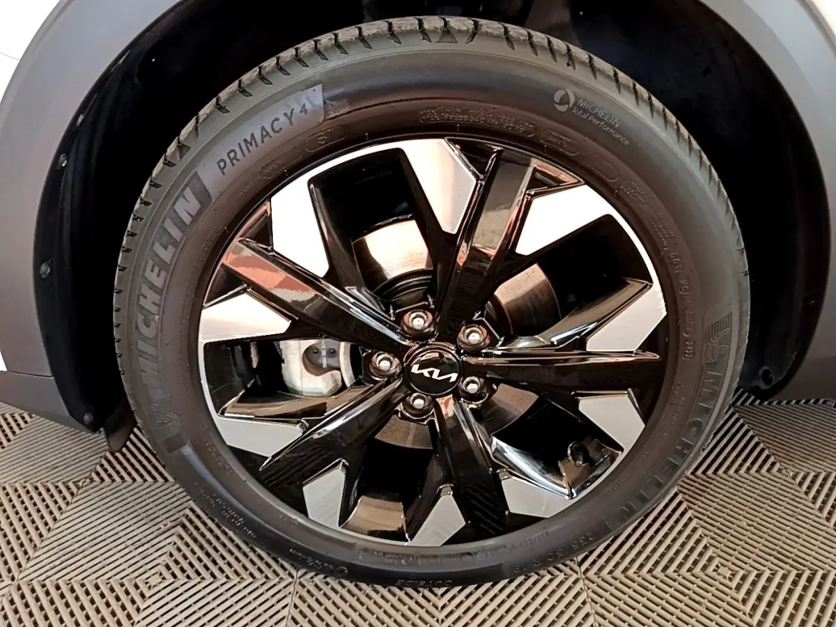 Gros plan sur la roue avant droite du KIA SPORTAGE blanc, jante alliage noir brillant avec logo KIA central.