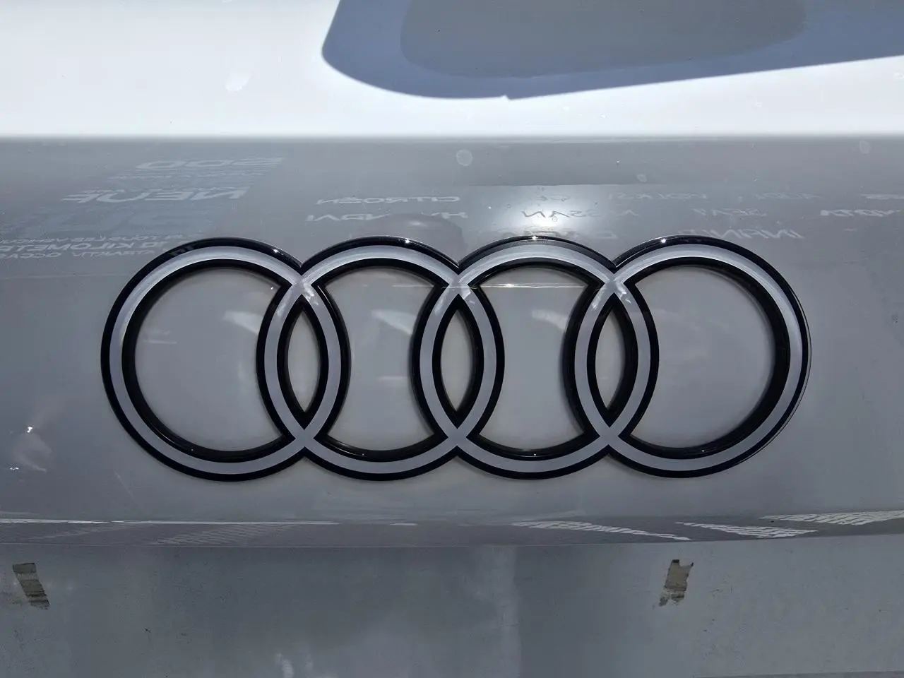 Gros plan sur le logo Audi noir brillant sur la carrosserie blanche Arkona d'une Audi A3 Sportback 2024.