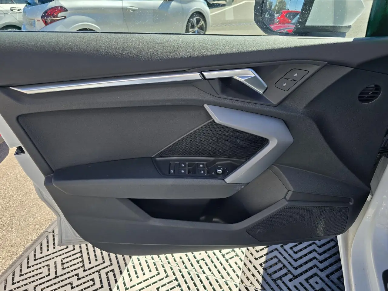 Vue intérieure du panneau de porte côté conducteur de l'Audi A3 blanc Arkona avec commandes électriques et poignée argentée.