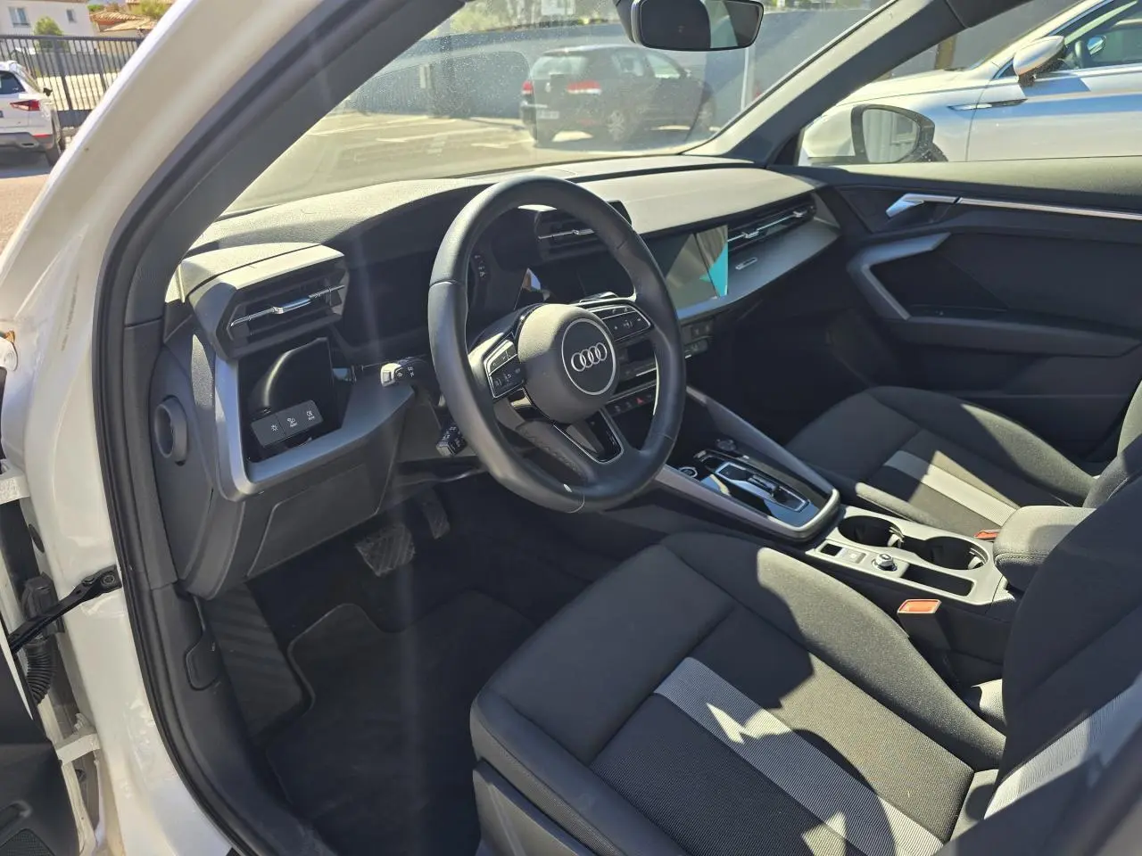 Vue intérieure côté conducteur de l'Audi A3 Sportback 2024 avec sièges noirs et volant multifonctions en cuir.