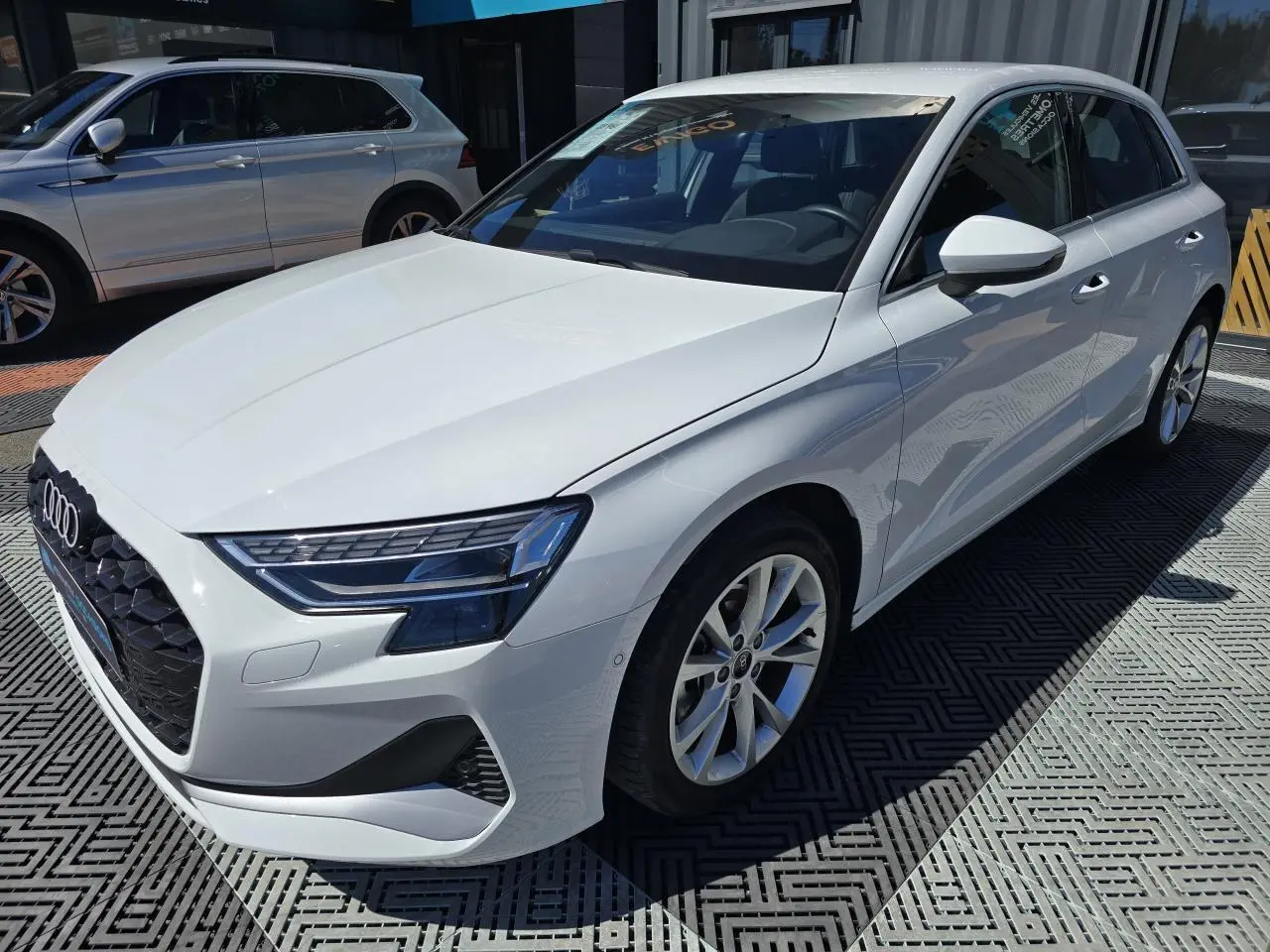 Audi A3 Sportback blanc Arkona vue 3/4 avant droit, avec jantes alliage 5 branches et phares LED distinctifs.