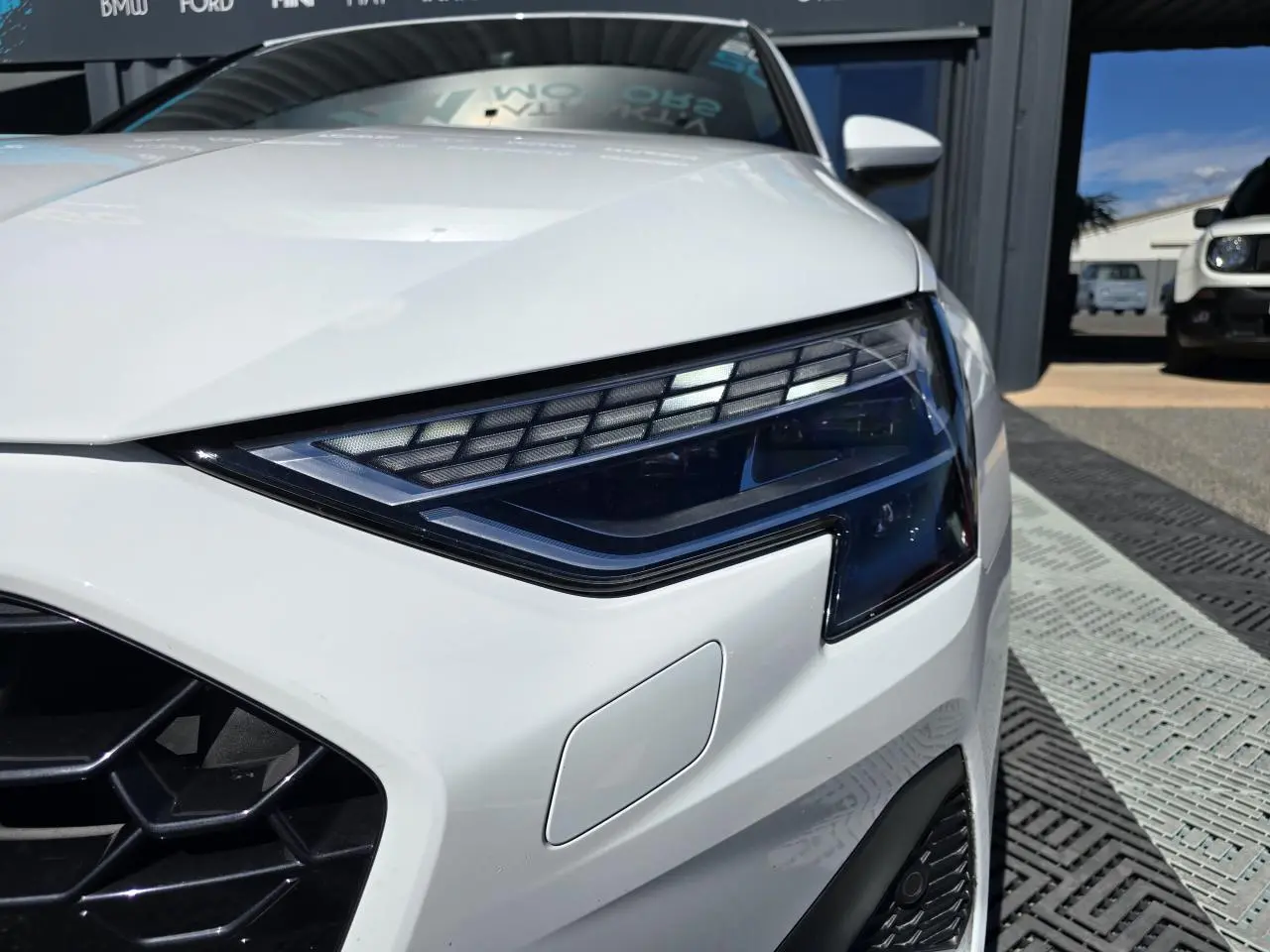 Gros plan sur le phare avant droit blanc Arkona d’une Audi A3 Sportback 2024 avec calandre noire et détails LED.