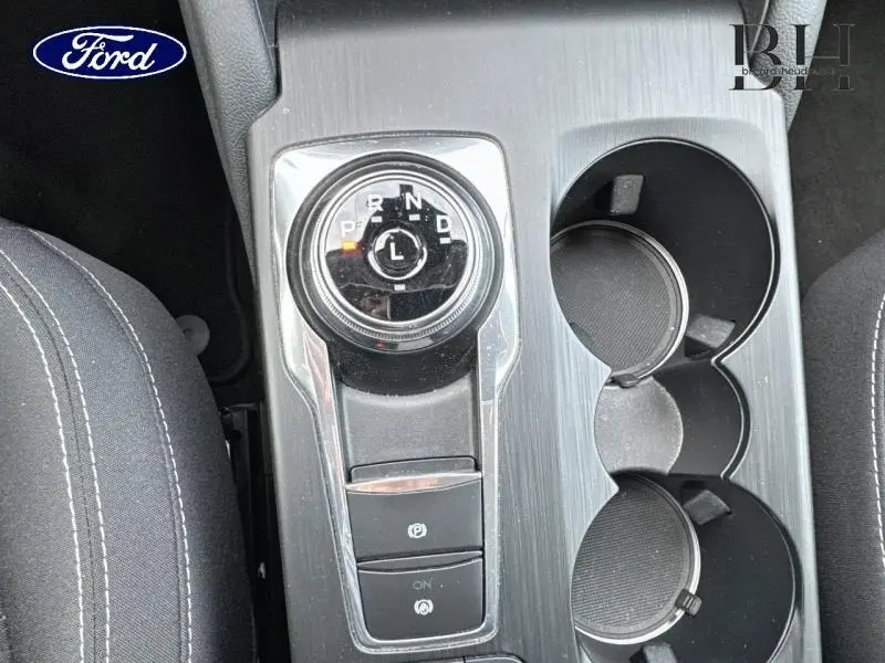 Gros plan sur la console centrale du Ford Kuga blanc, montrant la molette de boîte auto et les porte-gobelets noirs.