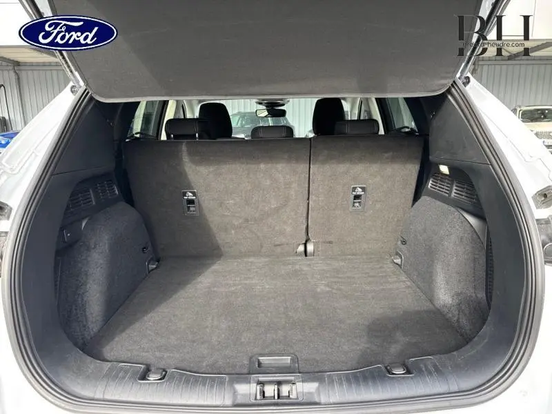 Coffre ouvert vu de l'arrière du Ford Kuga blanc Glacier 2021, avec banquette arrière relevée et tapis noir.