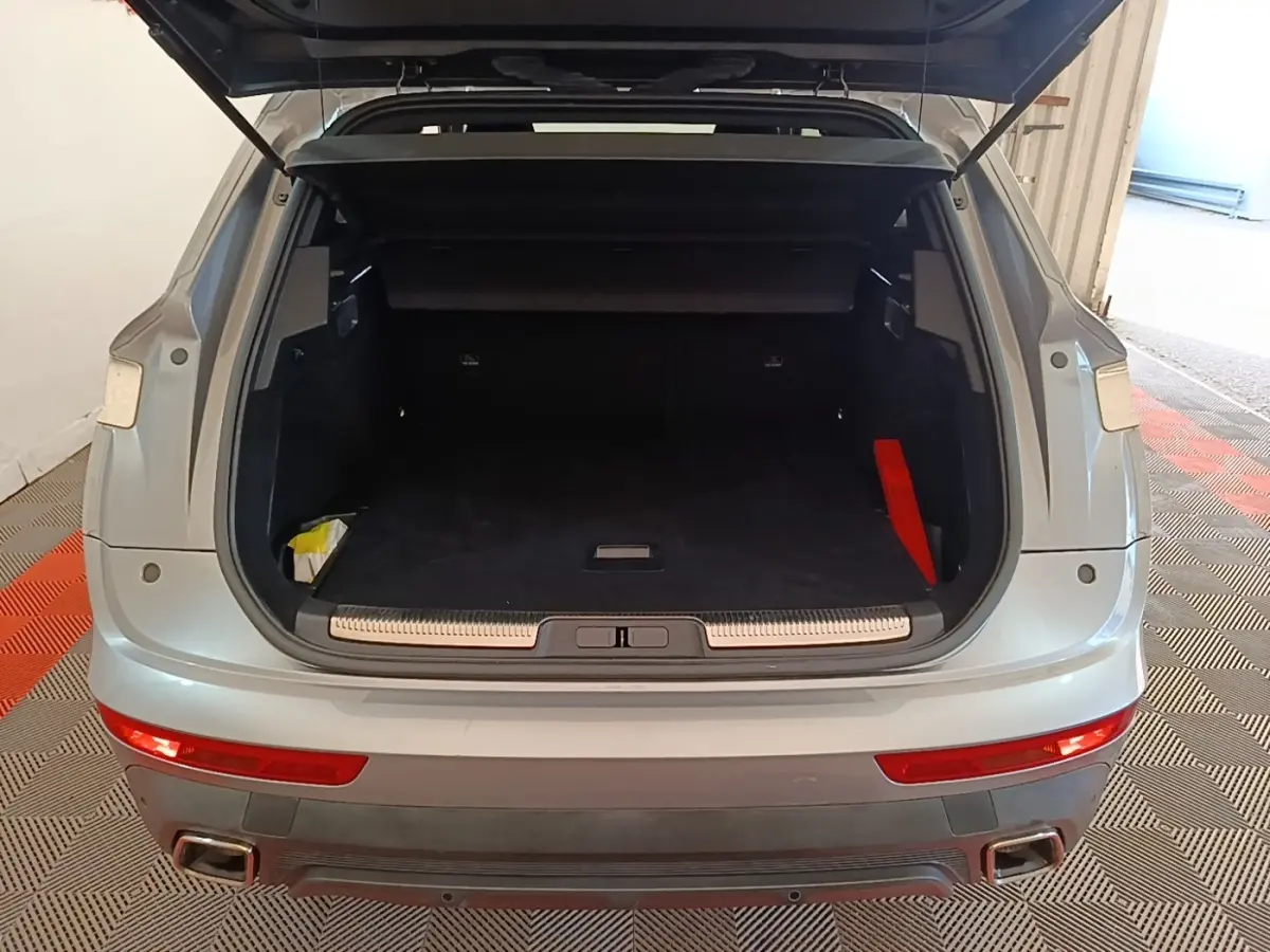 Vue arrière du coffre ouvert du DS7 Crossback gris foncé, montrant l'espace de chargement vide et les feux arrière allongés.