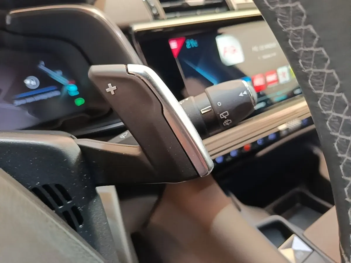 Gros plan sur la palette de changement de vitesse au volant cuir du DS7 Crossback gris foncé, tableau de bord numérique en arrière-plan.