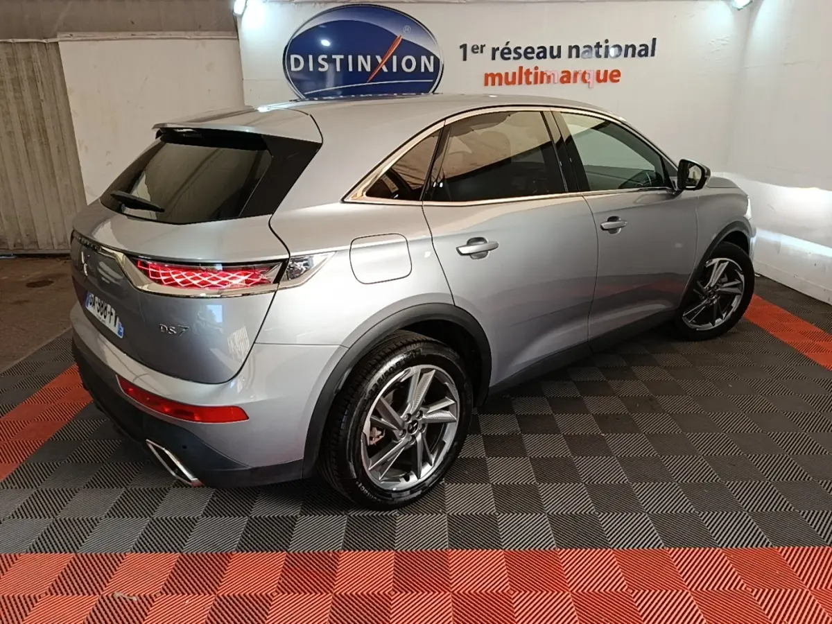 Vue 3/4 arrière droite du DS7 Crossback E-TENSE 225 Business gris foncé avec feux arrière LED allumés en intérieur showroom.