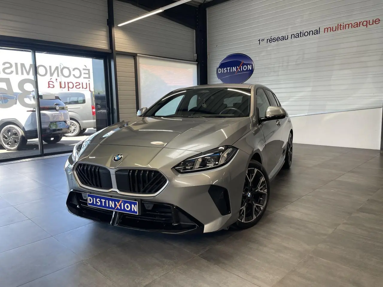 BMW Série 1 120d M Sport gris en 3/4 avant dans un showroom avec jantes 18 pouces bicolores et calandre noire.