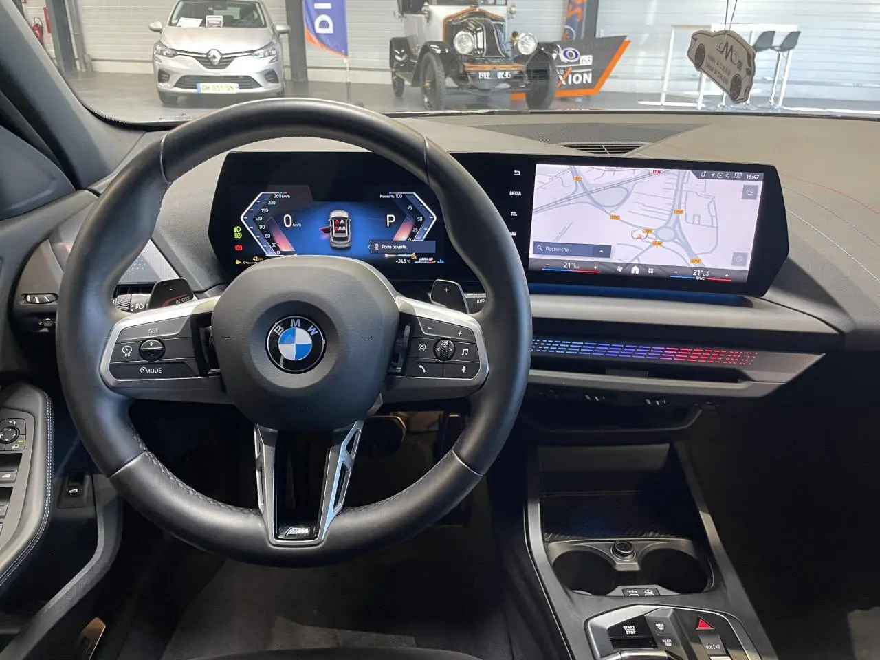 Vue intérieure centrée sur le volant cuir M et le BMW Curved Display avec navigation, ambiance lumineuse M Sport visible.