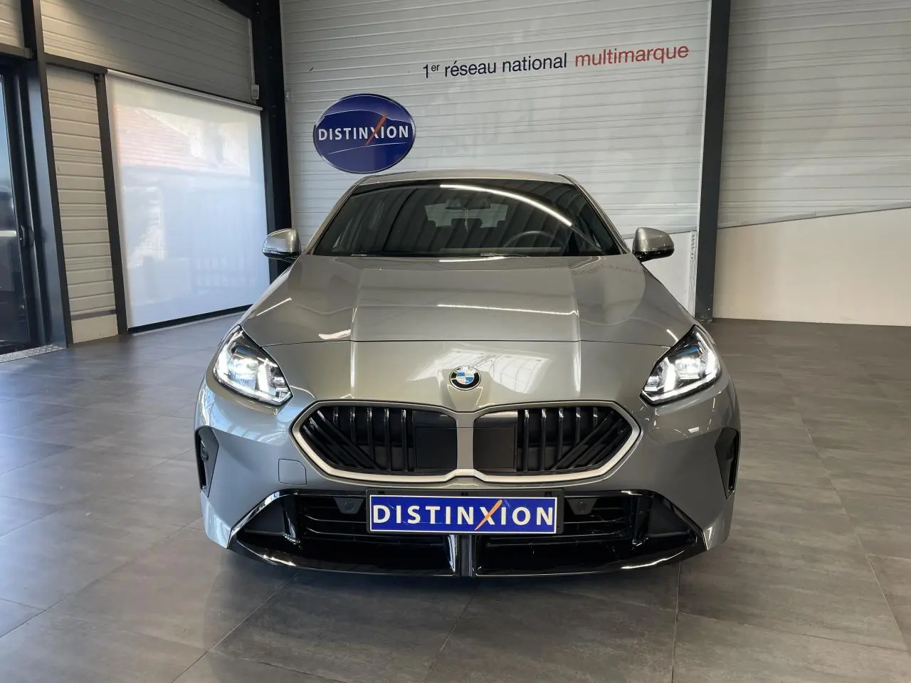 Vue frontale d'une BMW Série 1 120d M Sport gris avec calandre noire et projecteurs LED allumés en showroom.