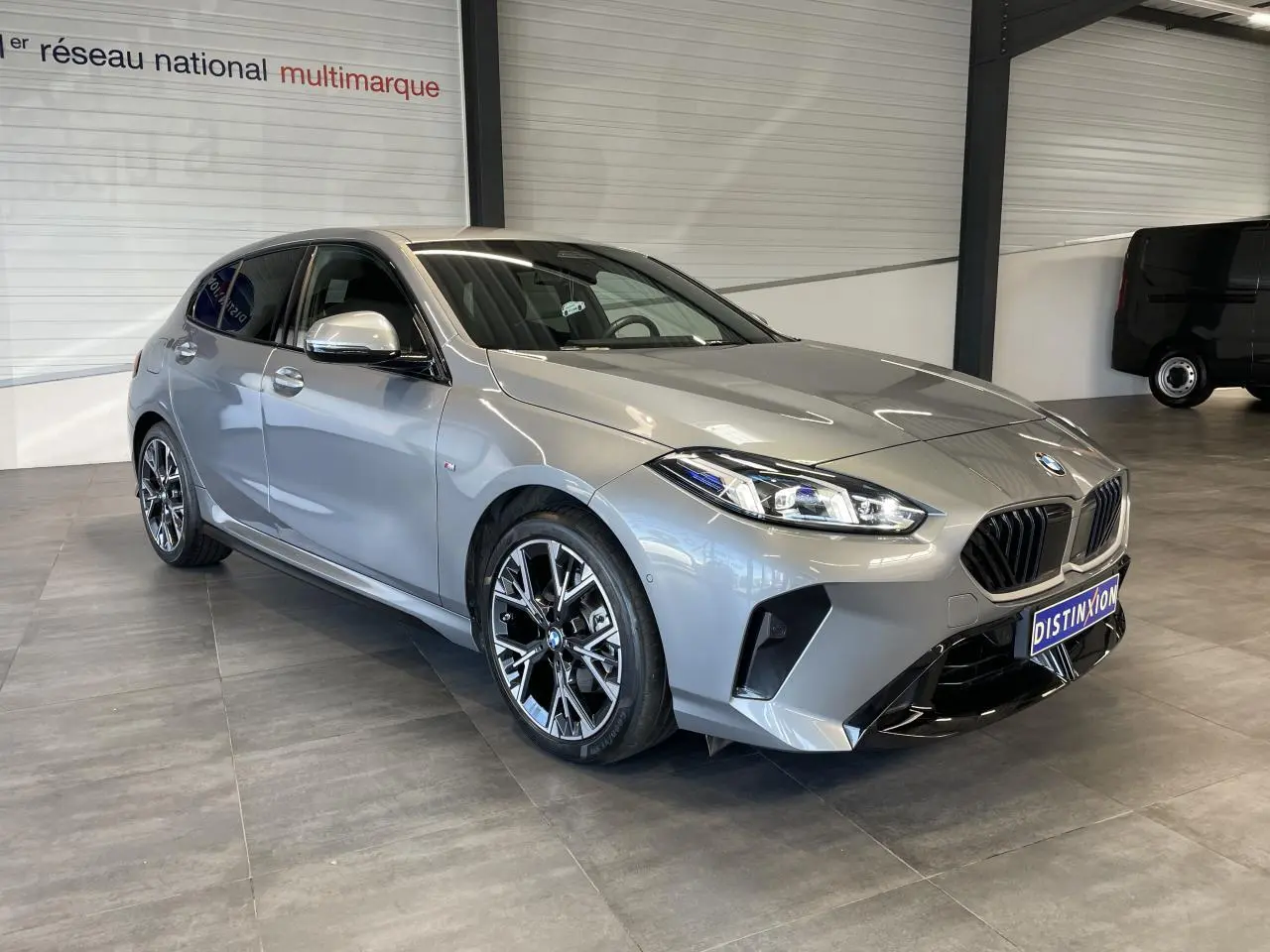 BMW Série 1 120d M Sport gris vue 3/4 avant droit, avec jantes bicolores et calandre noire sportive.
