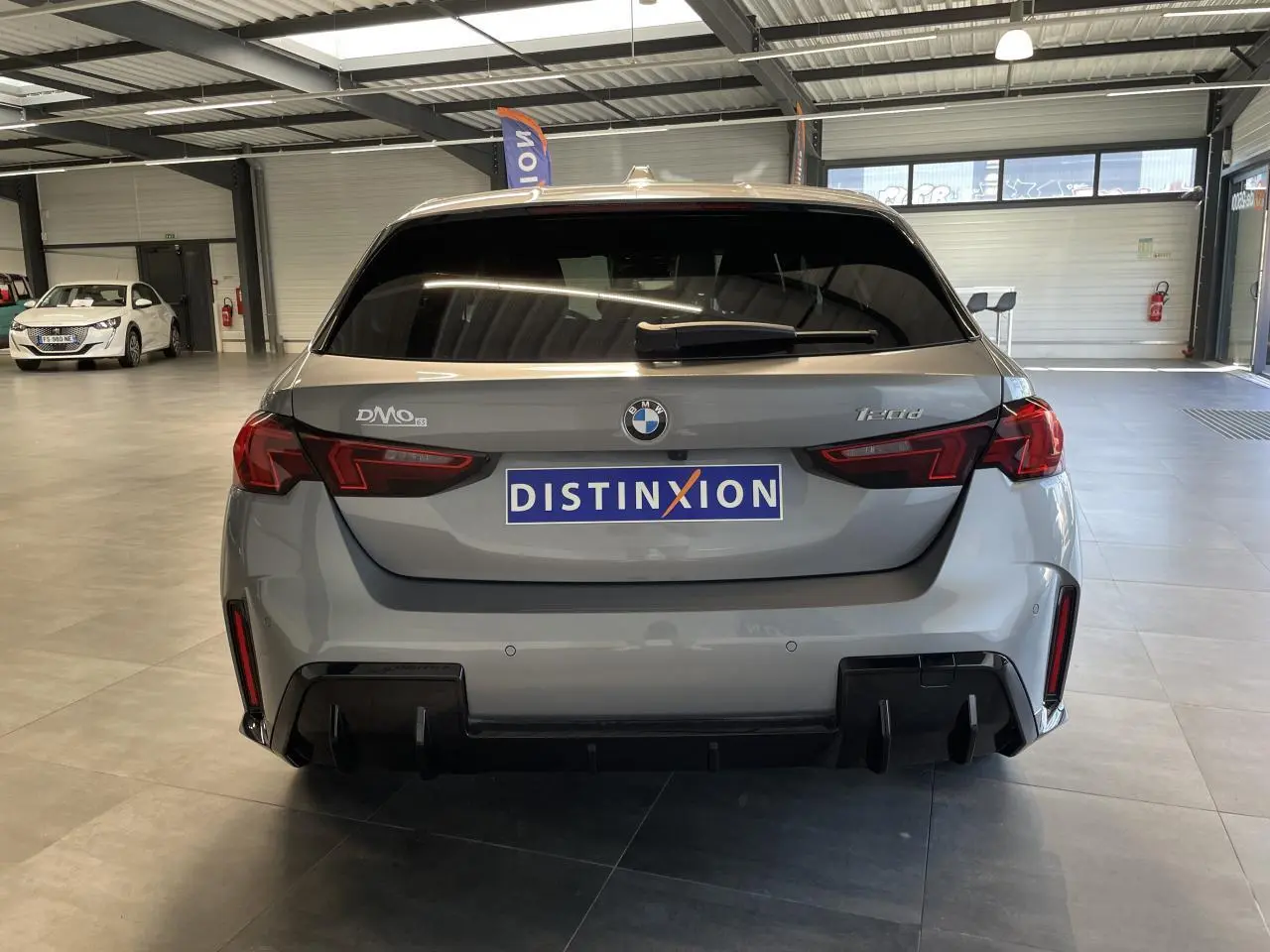 Vue arrière d'une BMW Série 1 120d gris avec diffuseur noir et feux LED en intérieur showroom.