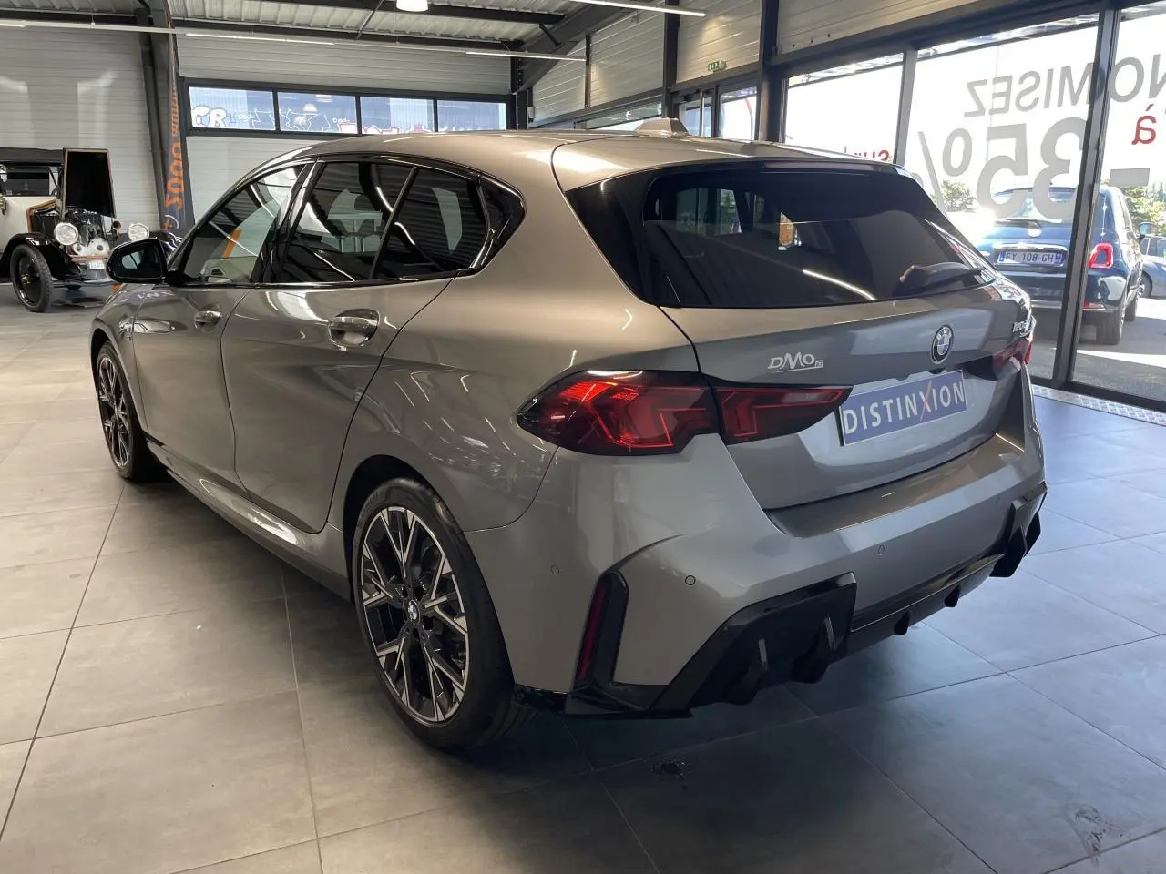 BMW Série 1 120d M Sport gris vue 3/4 arrière droit en intérieur avec jantes bicolores et diffuseur noir M Sport.