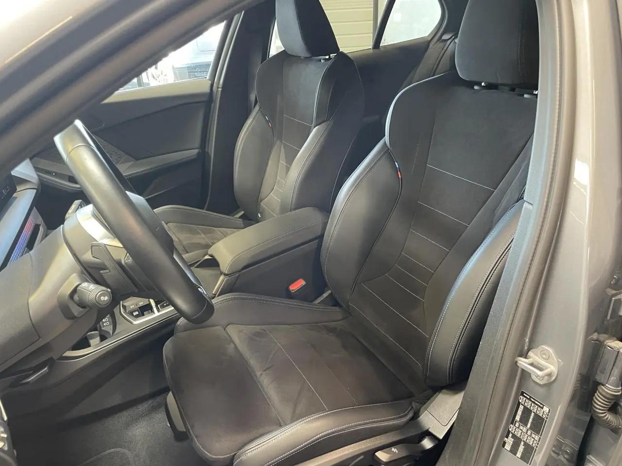 Vue intérieure côté conducteur de la BMW Série 1 120d M Sport 2025 avec sièges sport Alcantara noirs et surpiqûres bleues.