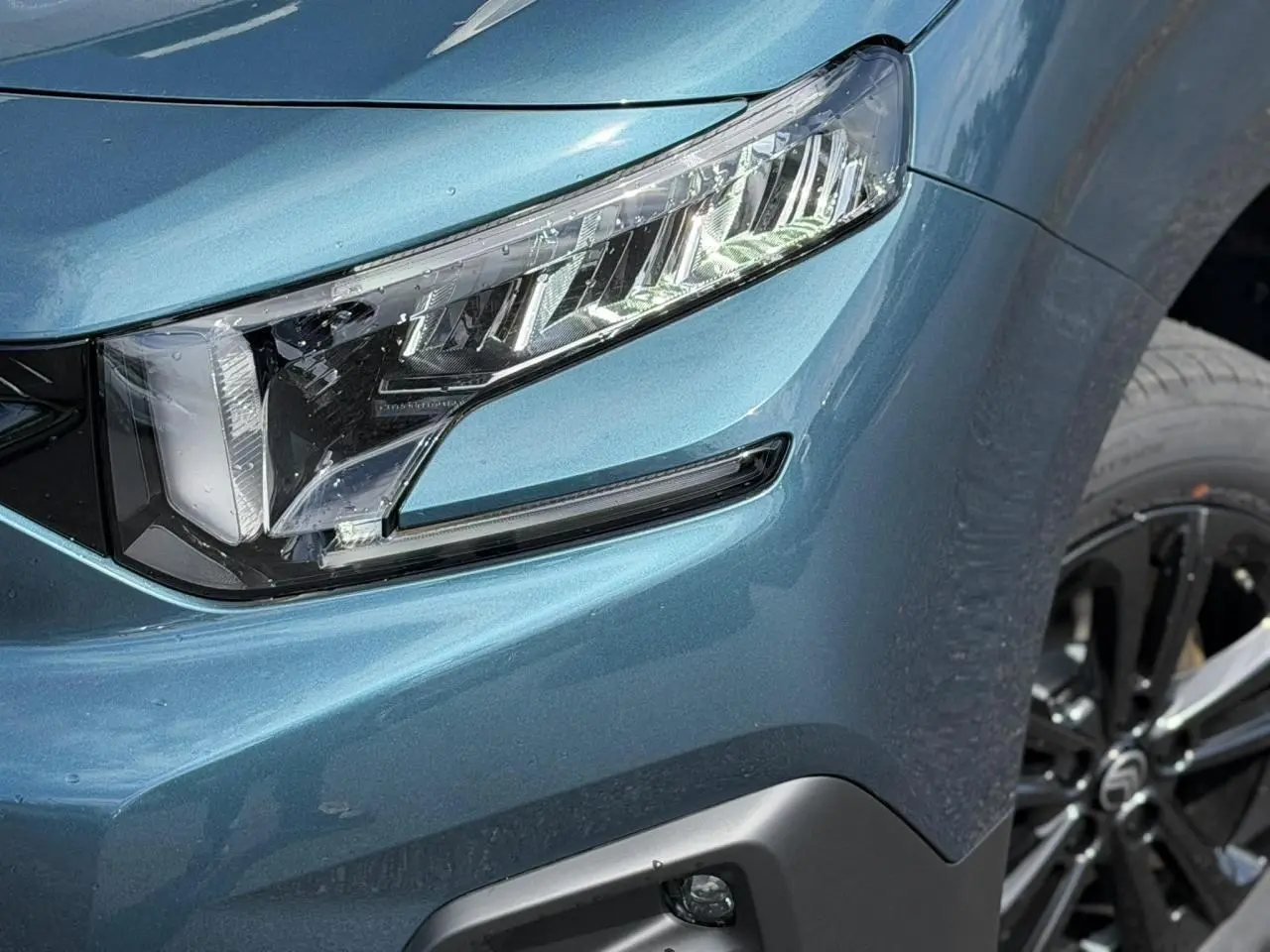 Gros plan sur le phare avant droit et la jante alliage noire du Citroën Berlingo Multispace Bleu Kiama métallisé.