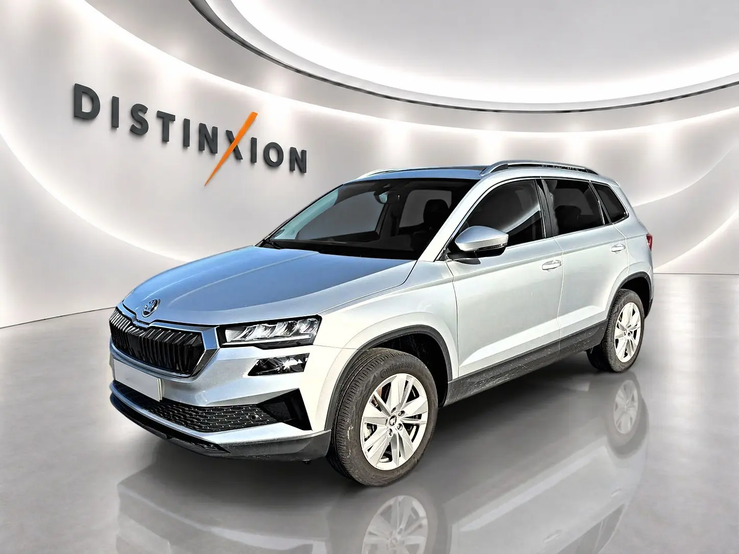 Vue 3/4 avant droite d'un Skoda Karoq gris 2025 avec calandre noire et jantes alu cinq branches.