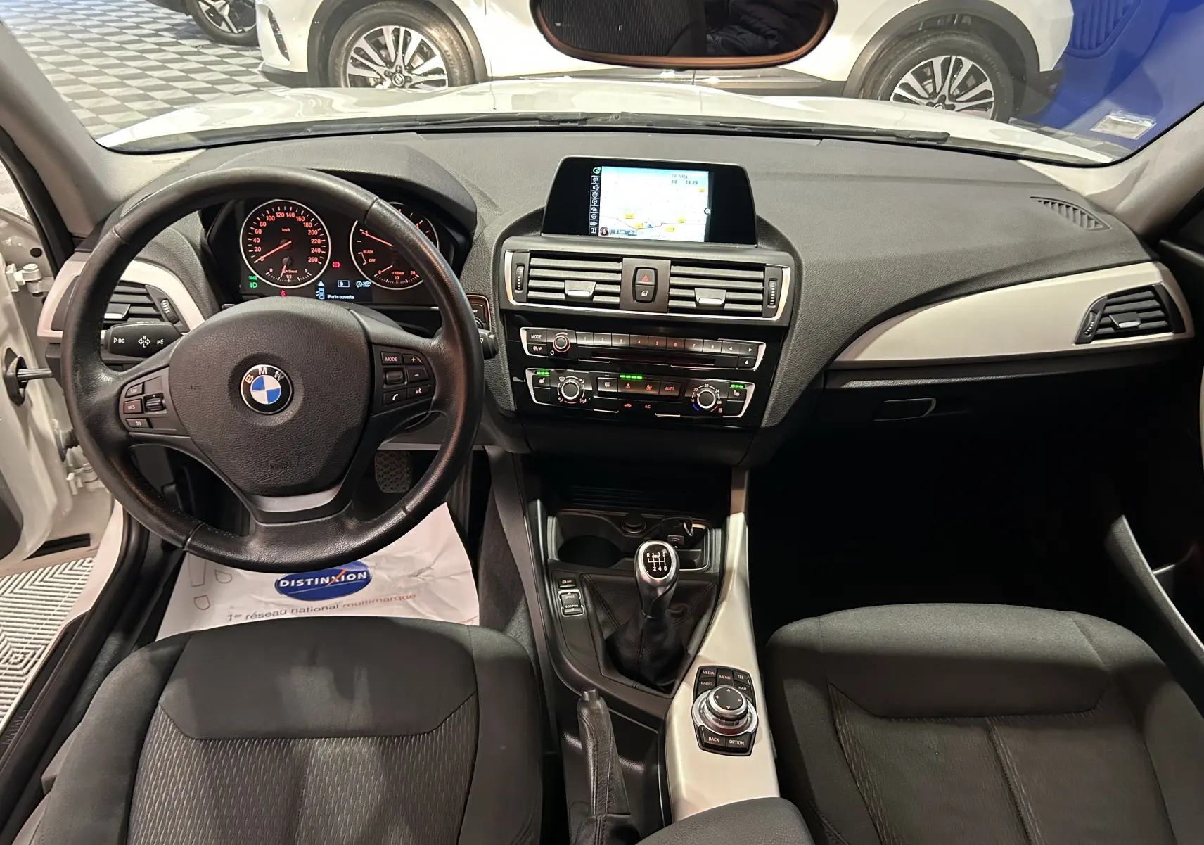 Vue intérieure de la BMW Série 1 116d Business 2015, tableau de bord noir avec écran central et boîte manuelle.
