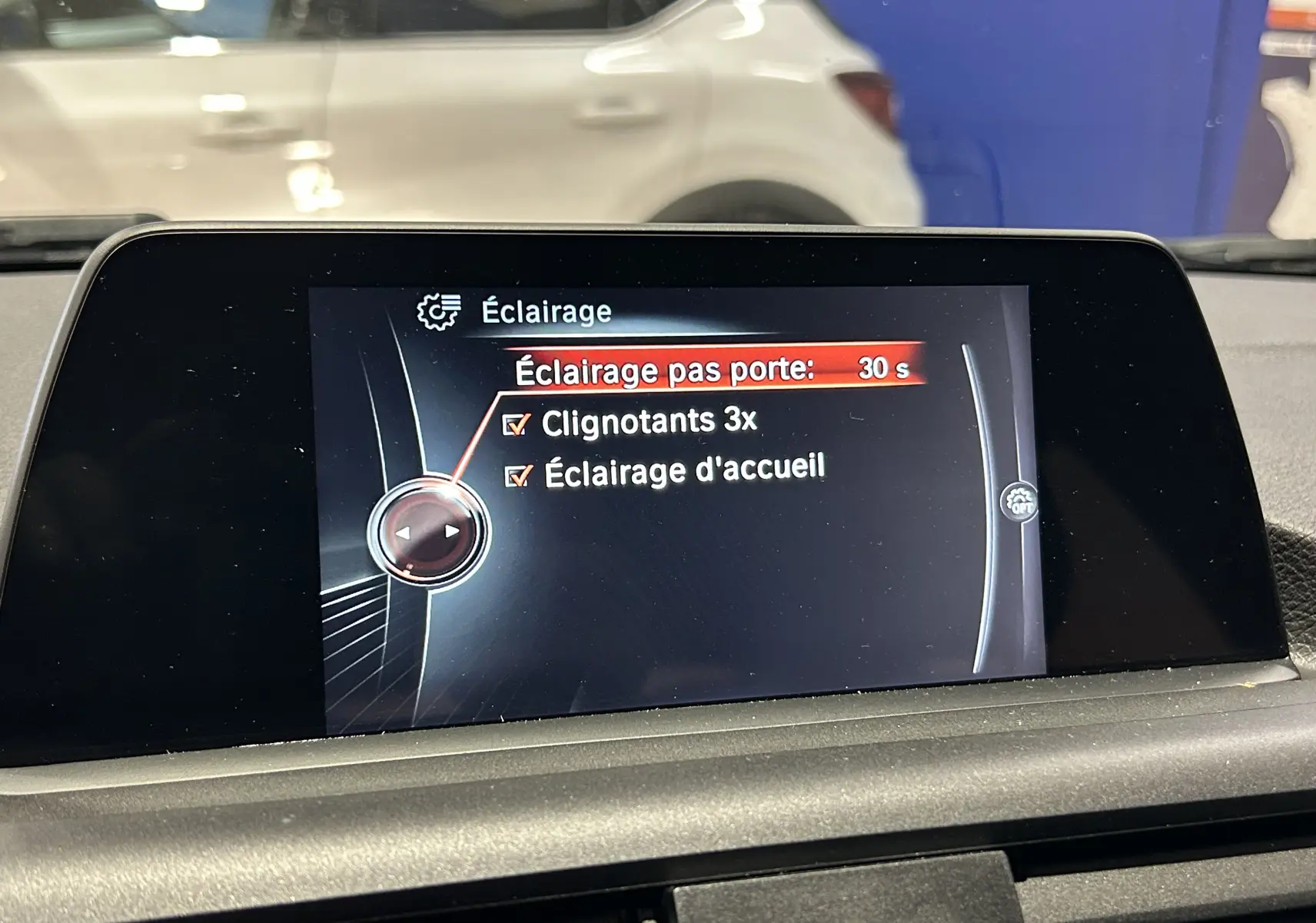 Écran central de la BMW Série 1 116d blanc montrant le menu éclairage avec options clignotants et accueil activées.