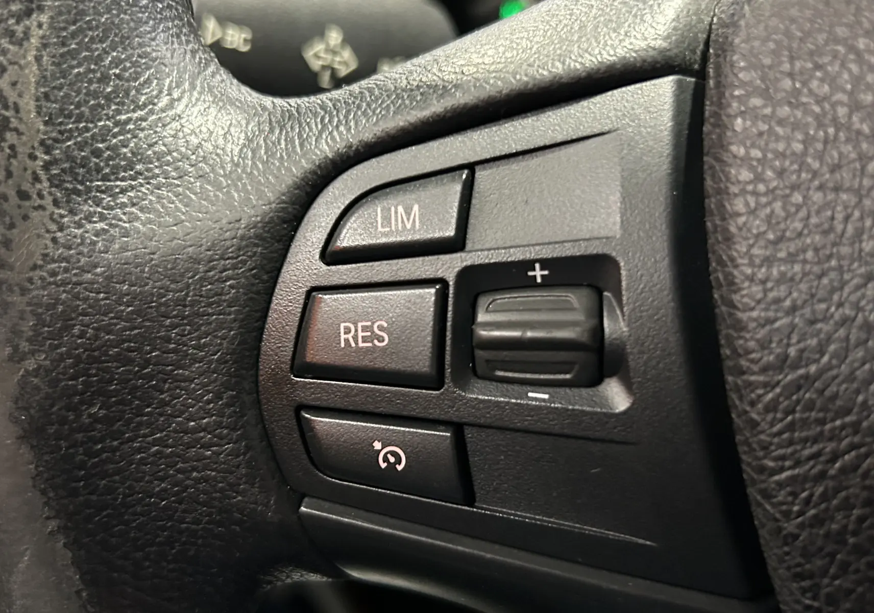 Gros plan sur les boutons de commande du régulateur de vitesse au volant en cuir noir d'une BMW Série 1 blanche 116d Business 2015.